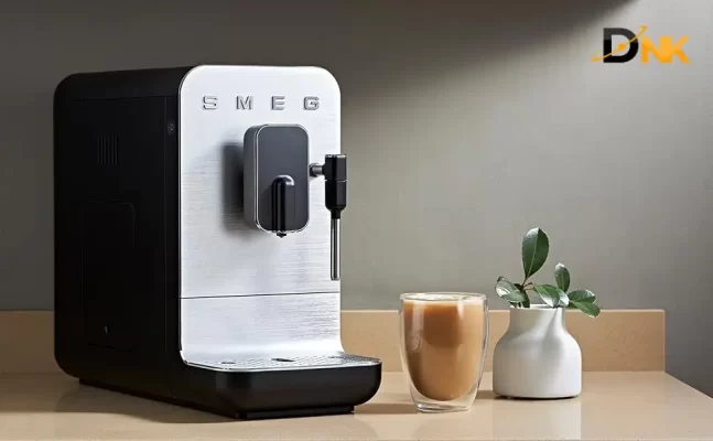 Máy Smeg Bcc12Blmeu Trên Bàn Bếp, Cạnh Ly Latte Và Bình Hoa, Ánh Sáng Chiếu Từ Trên Xuống