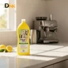 Chai Dung Dịch Denkmit Entkalker Trên Mặt Bàn Bếp, Phía Sau Là Ấm Đun Nước Và Máy Pha Cà Phê. Khả Năng Sử Dụng Cần Đối Chiếu Với Hướng Dẫn Của Từng Thiết Bị. Chai Denkmit Entkalker Đặt Cạnh Ấm Đun Nước Và Máy Pha Cà Phê
