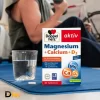 Hình Ảnh Minh Họa Hộp Doppelherz Magnesium Calcium D3 40 Viên Đặt Trên Thảm Tập, Cạnh Ly Nước Và Một Viên Nén, Với Người Đang Tập Tạ Ở Phía Sau. Hộp Doppelherz Magnesium Calcium D3 Bên Ly Nước Và Viên Nén Trên Thảm Tập