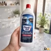 Hình Minh Họa Một Bàn Tay Cầm Chai Dung Dịch Vệ Sinh Lò Nướng Denkmit, Phía Sau Là Không Gian Bếp Và Cửa Sổ. Nhãn Trước Thể Hiện Tên Denkmit Backofen- Und Grillreiniger Gel. Tay Cầm Chai Dung Dịch Vệ Sinh Lò Nướng Denkmit Trong Không Gian Bếp