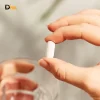 Bàn Tay Cầm Viên Nén Màu Trắng Hình Thuôn Dài Bên Cạnh Ly Nước.